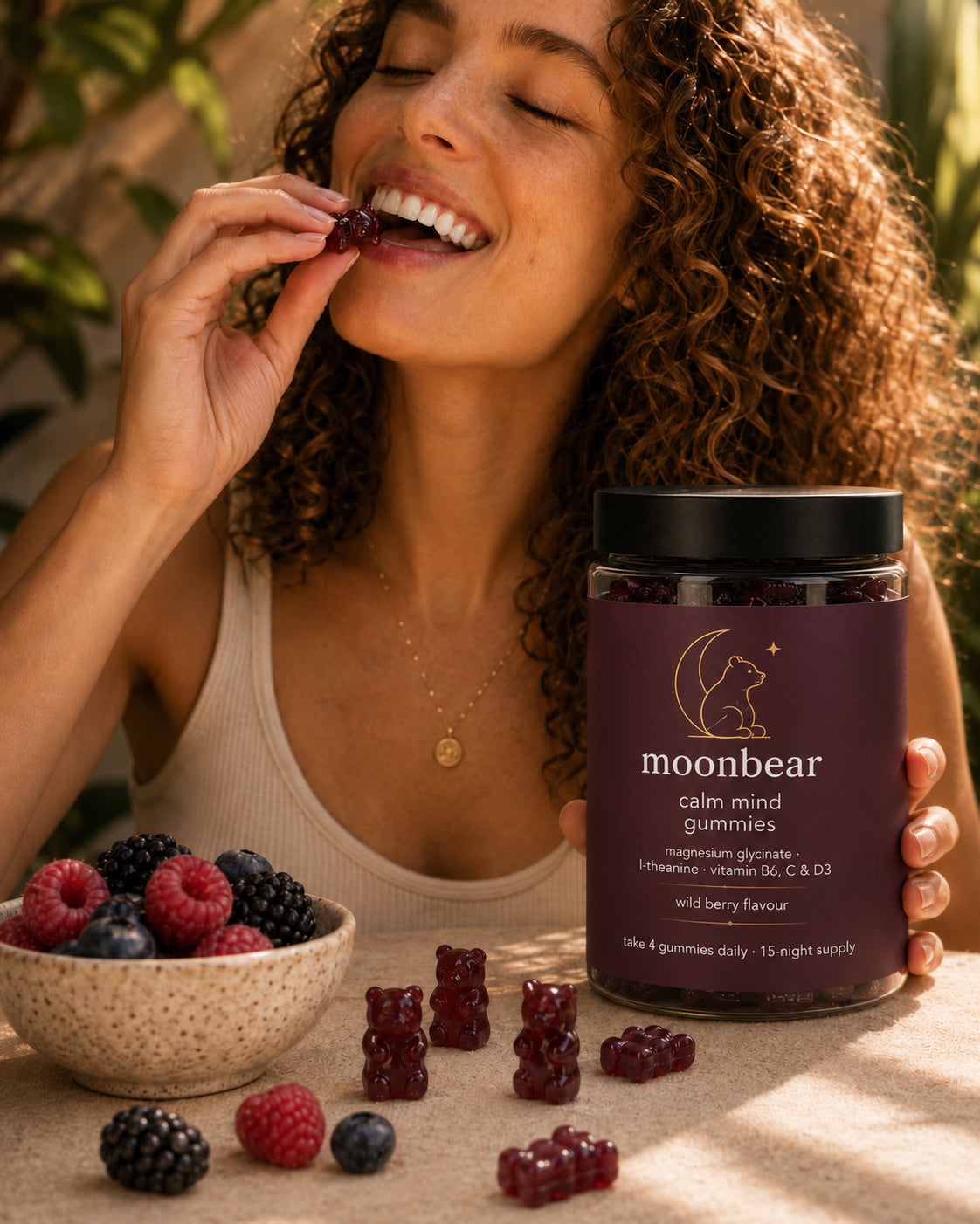 Woman enjoying a moonbear wild berry gummy in warm natural light, jar in hand beside a bowl of berries